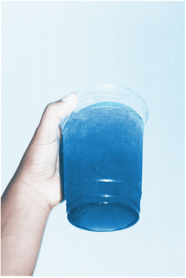 a hand holding a glass of blue up to the sky